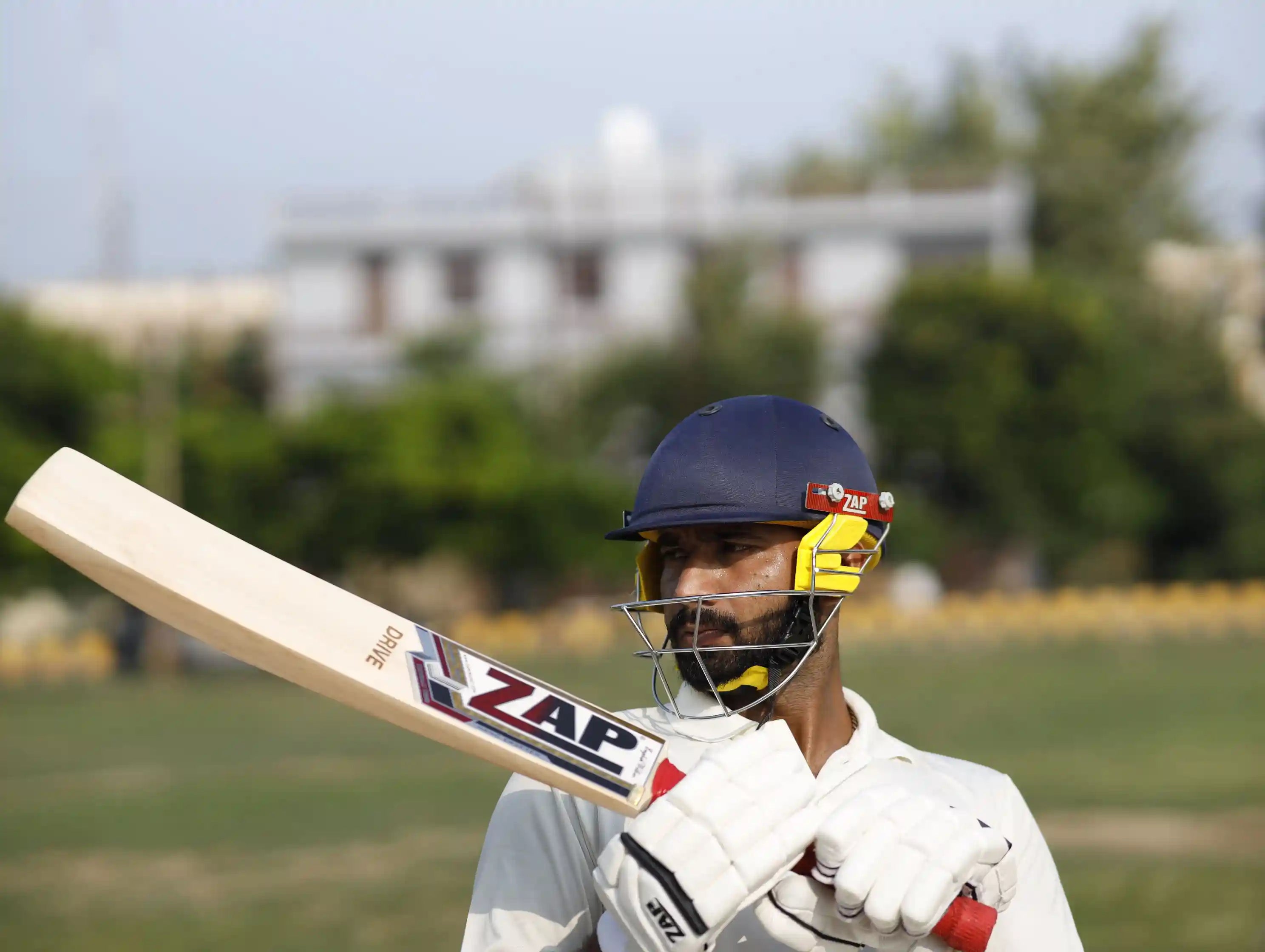 Playing holding a cricket bat while wearing gloves and helmet