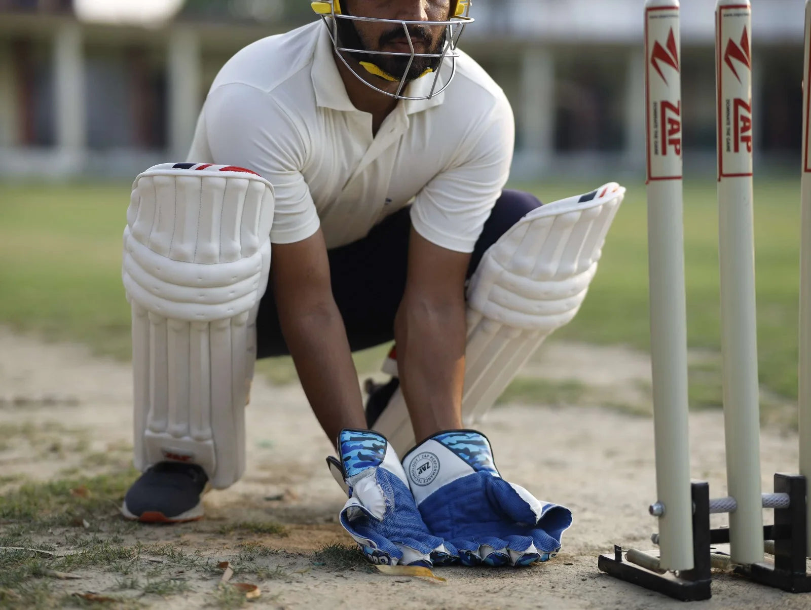 A wicket keeper in the squat wicket keeping position behind the stumps, wearing the ZAP Wicket Keeping kit